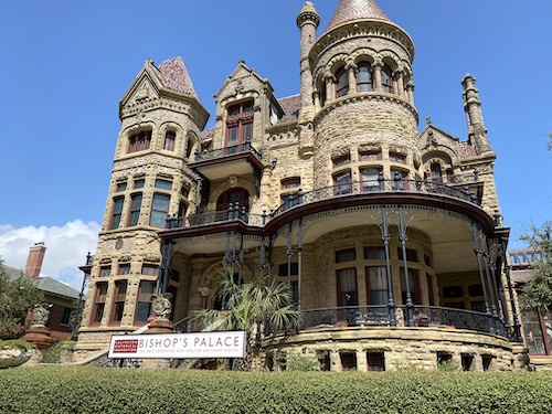 Photo of Bishop's Palace from front of building. Shows 4 stories of stone structure with a large porch rounded on the right side, round structure above it, and sign in front saying "Bishop's Palace." 