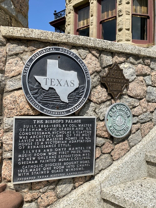 Phot shows rock wall outside of the building (top part of photo shows partial wall and balcony of building. The rock wall shows 4 markers: The Texas State Historical Medallion, the "1900 Surviver Storm" bronze marker, the circular Galveston Landmark marker, and the rectangular marker showing it is a recorded Texas Historic Landmark, dedicated in 1967. This marker says, "The Bishop's Palace." Built, 1886-1893, by Col. Walter Gresham, Civic leader and U.S. Congressman. Nicholas J. Clayton was architect. One of the most lavish and massive homes in U.S., house is a Victorian adaptation of Renaissance style. Silver and Onyx mantel in music room won first prize, 1886, at New Orleans Exposition. Mrs. Gresham painted murals, ceilings. Catholic Diocese bought home, 1923, made one room into chapel with stained glass windows."