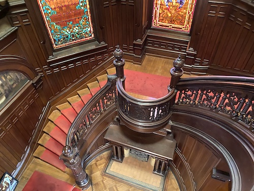 Photo os taken from the second floor looking down on the mahongany staircase and fireplace, as well as the two stained glass windows. 