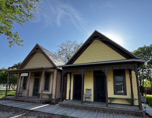 Two single-story old houses. ONe is yellow with brown trim, the other is tan with brown trim.
