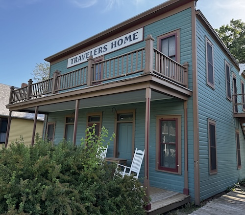 Two story green building with sign saying Travelers Home.