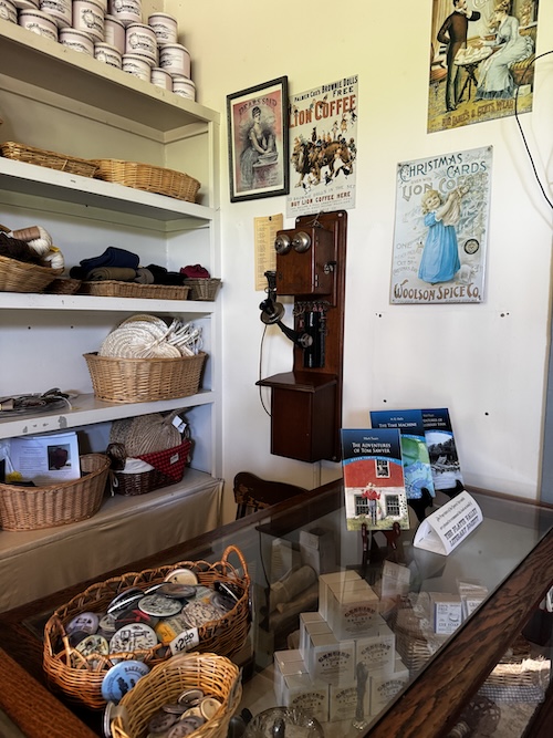 Inside of store, showing old telephone, wall advertisements, baskets with items for sale.