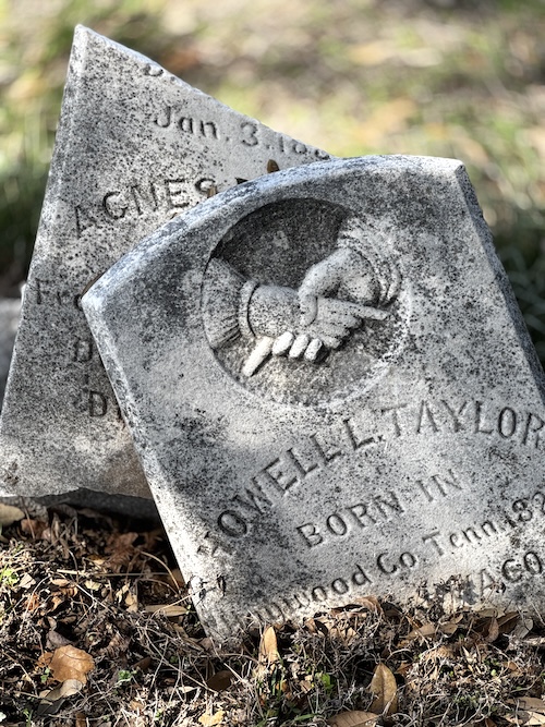 Image of a broken upright headstone, one piece sitting in front of the other.